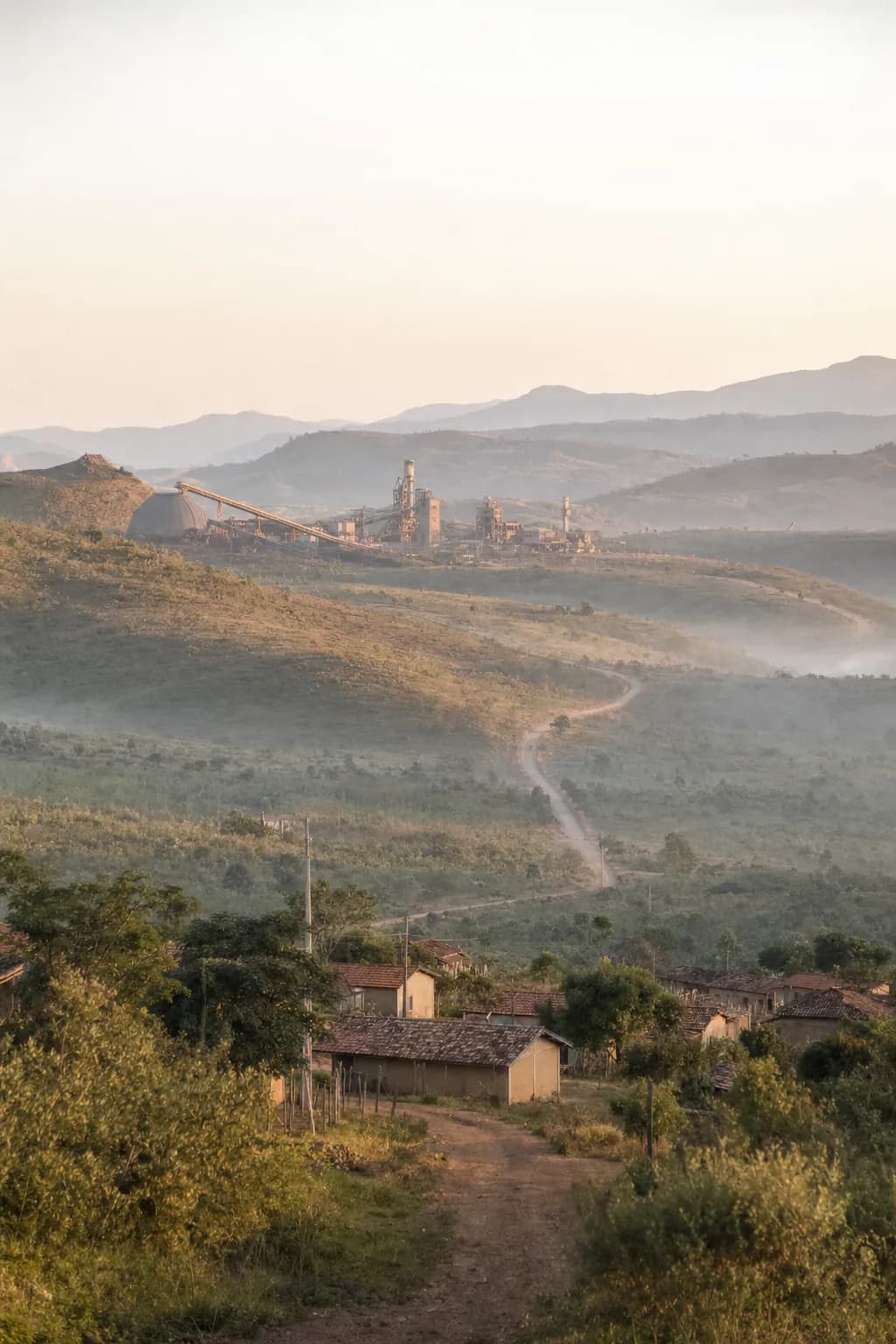 Valley with a small rural community in the foreground and mining structures far off on the horizon, under late-afternoon light
